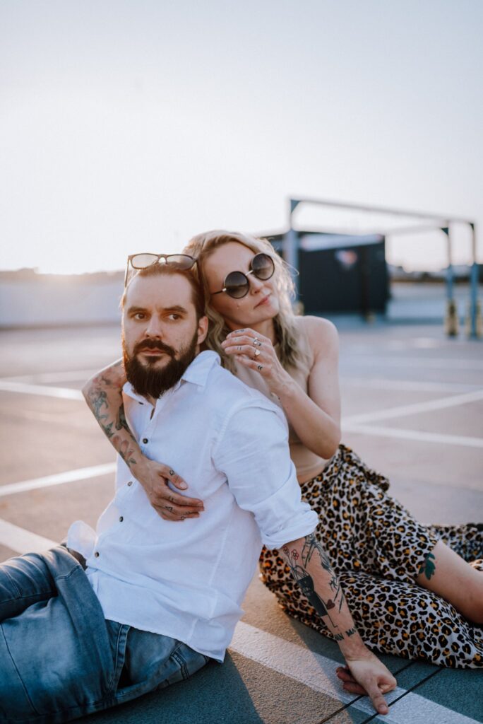 para siedząca na ziemi i przytulająca się na parkingu na tle zachodzącego słońca