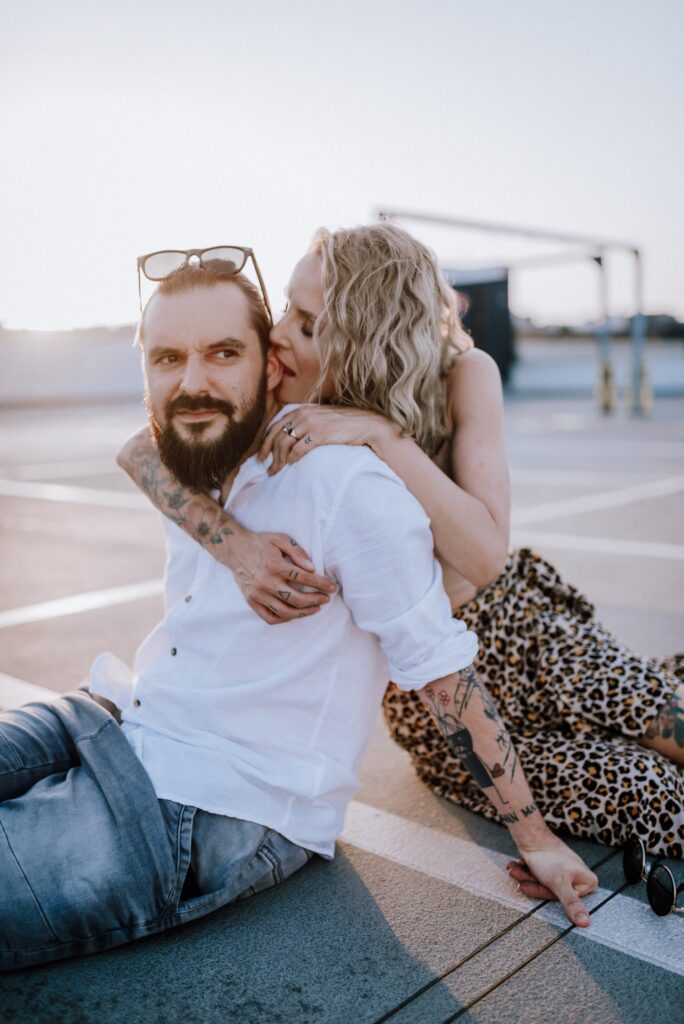 para siedząca na ziemi i przytulająca się na parkingu na tle zachodzącego słońca