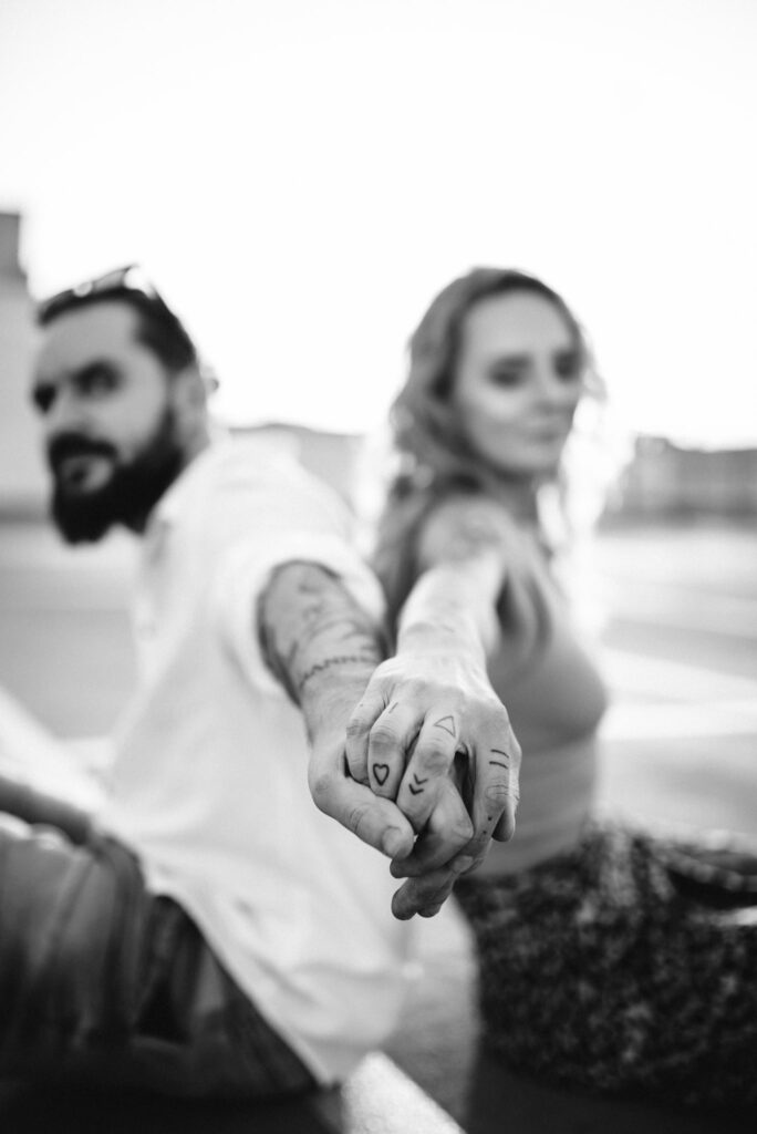 zbliżenie na splecione dłonie mężczyzny i kobiety z tatuażami w tle widać rozmytą parę