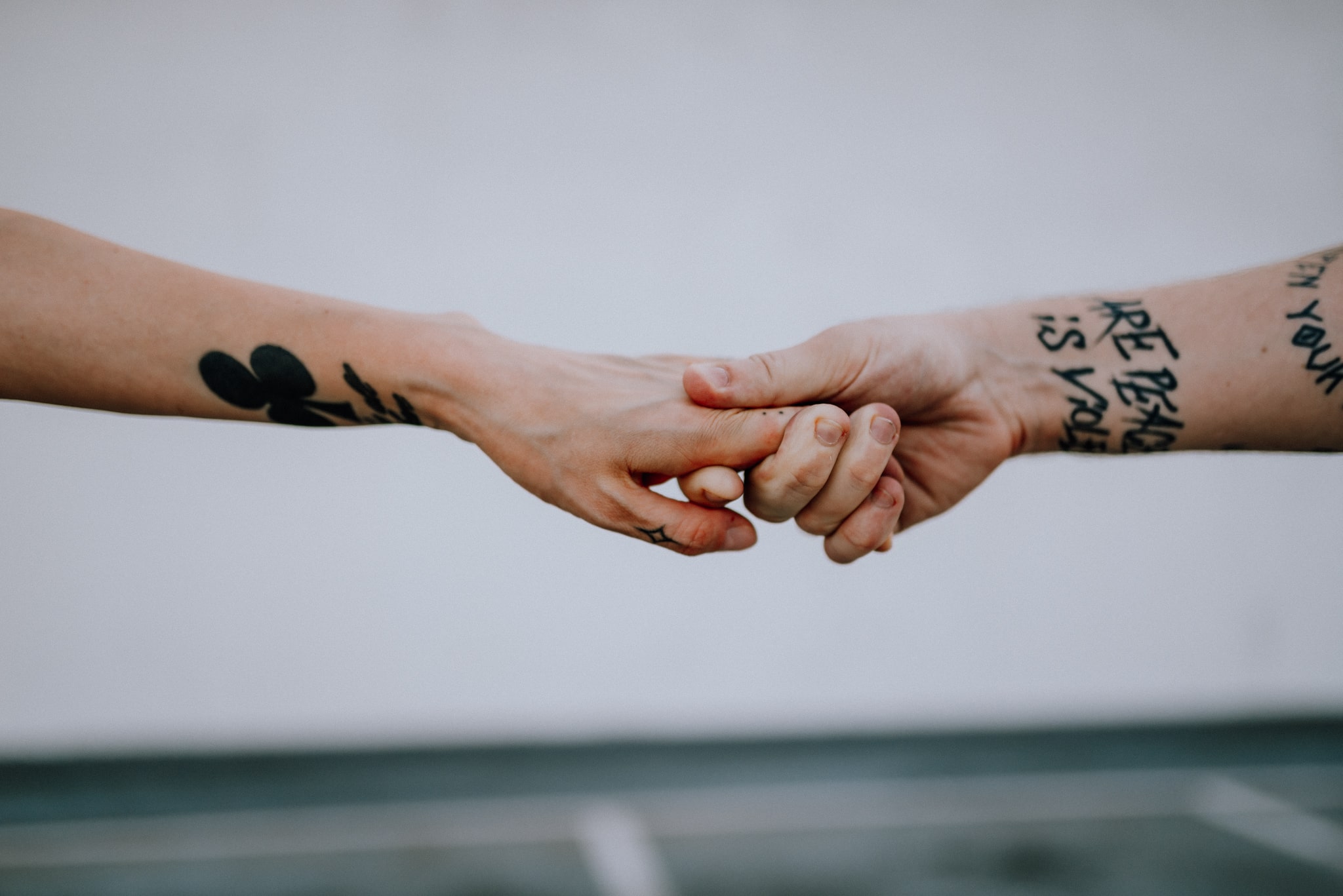 zbliżenie na trzymające się dłonie, powyżej nadrgarstków widoczne są tatuże