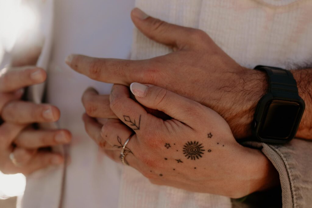 zblizenie na dłonie męską i damską ze splecionymi palcami, na dłoni kobiety są widoczne tatuaże