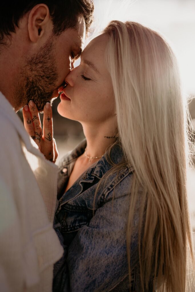 Zakochana para zbliżająca się do pocałunku podczas złotej godziny, sesja narzeczeńska na plaży.