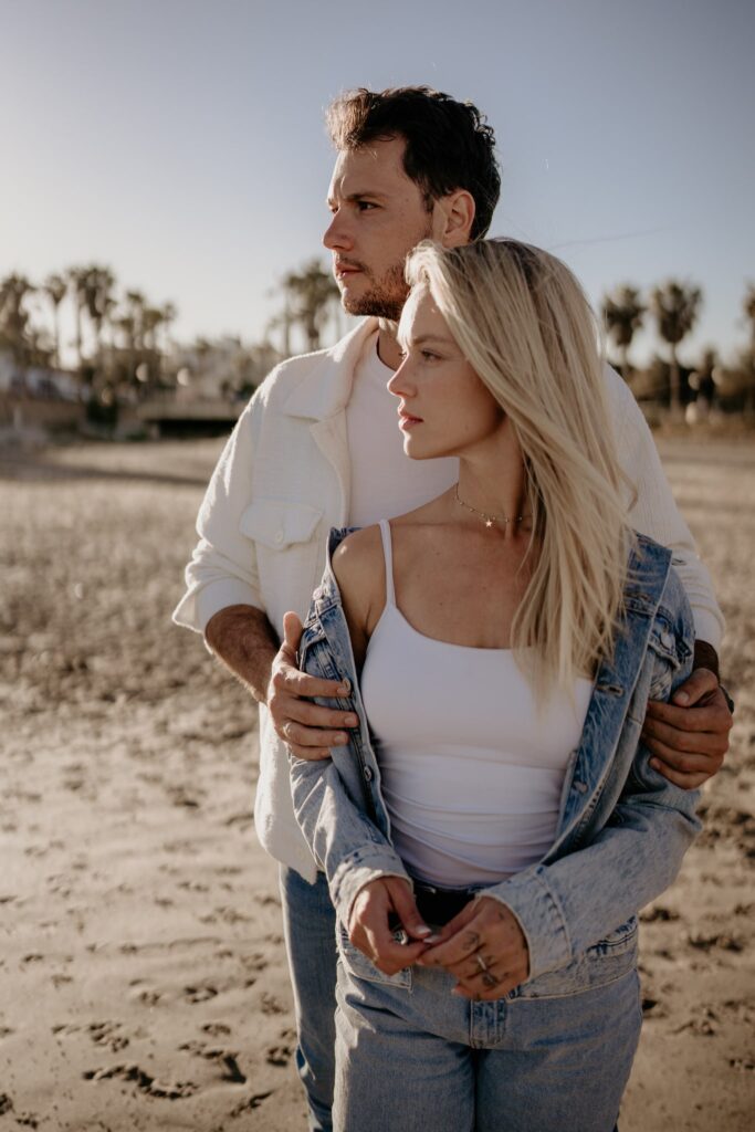 Para na plaży w Torrevieja, ubrana w jeansy i jasne kurtki. Mężczyzna obejmuje kobietę od tyłu, oboje patrzą na horyzont.