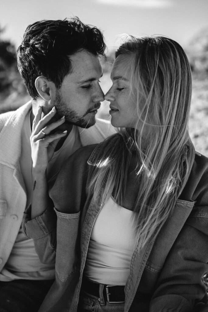 Czarno-biała fotografia pary w intymnym momencie, kobieta delikatnie trzyma mężczyznę za twarz podczas sesji narzeczeńskiej.