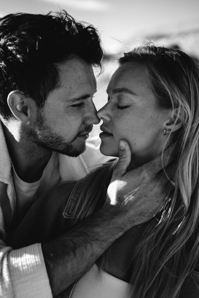 Czarno-biała fotografia pary w intymnym momencie, mężczyzna delikatnie trzyma kobietę za twarz podczas sesji narzeczeńskiej.