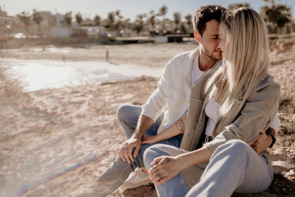 Para na plaży w Torrevieja, kobieta z długimi blond włosami, zwrócona jest w stronę mężczyzny, dotykają się czołami. W tle palmy i morze o złotej godzinie.